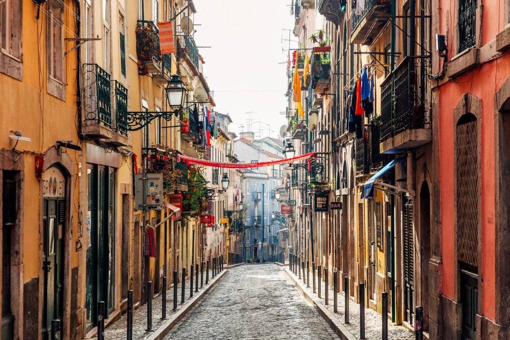 A quiet street in Lisbon's Bairro Alto district, featuring traditional Portuguese architecture with colorful buildings and narrow cobblestone lanes