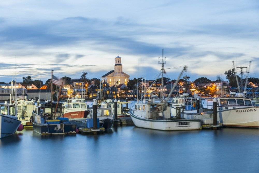A peaceful view of Provincetown Harbor with boats anchored in calm waters, surrounded by distant buildings and docks