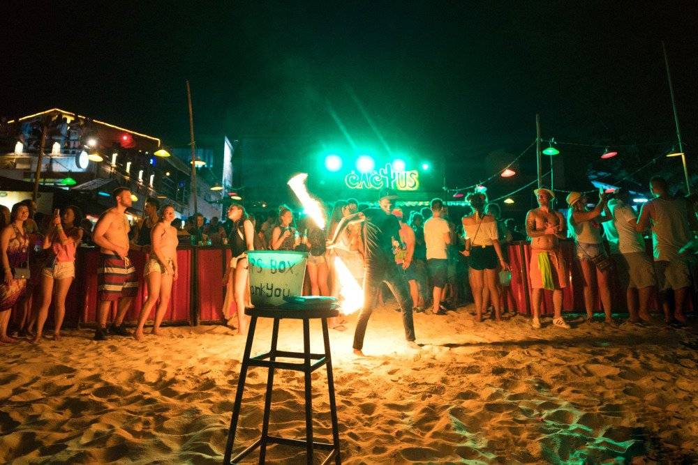 Partygoers dancing and enjoying the vibrant Full Moon Party under colorful lights on Koh Phangan beach at night.